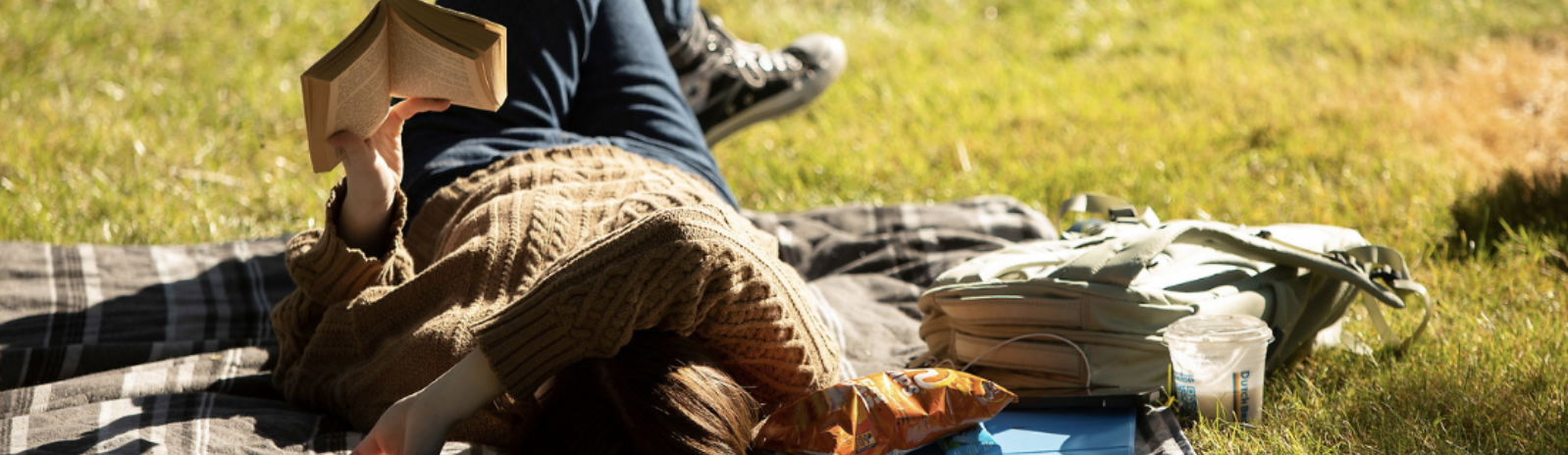 Student reading on a blanket in the grass